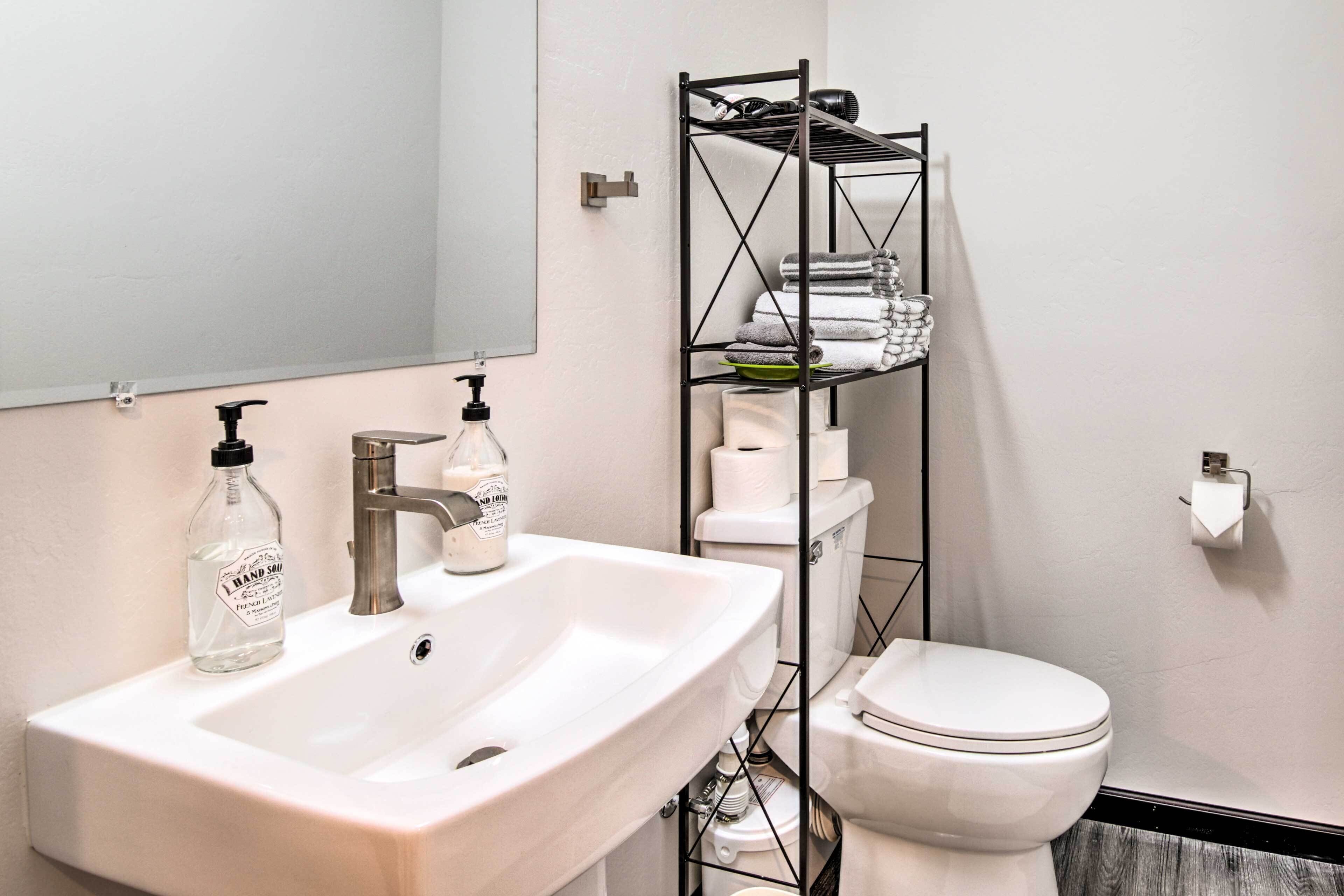 Ein Badezimmer mit einem weißen Waschbecken, einem Spiegel, einer Toilette und einem Metallregal mit Handtüchern und Pflegeprodukten.