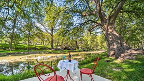 Une table de pique-nique avec deux chaises rouges et une bouteille de vin, le tout installé devant un étang bordé d’arbres.