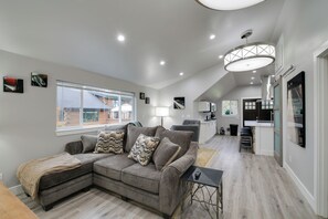 Ein modernes Wohnzimmer mit einer Eckcouch, einem kleinen Tisch und einer Küchenzeile im Hintergrund.