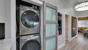 Une buanderie équipée d’une machine à laver et d’un sèche-linge superposés, d’une porte coulissante et d’un couloir menant à une chambre.