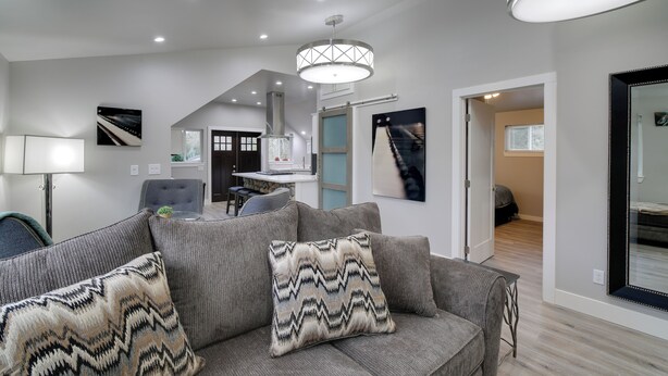 Un salon moderne avec un canapé gris, des coussins à motifs, un luminaire suspendu et un grand miroir.