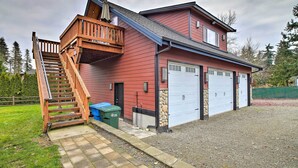 Une maison à deux étages avec un escalier en bois menant à un balcon, un mur d’accent en pierre et deux portes de garage.
