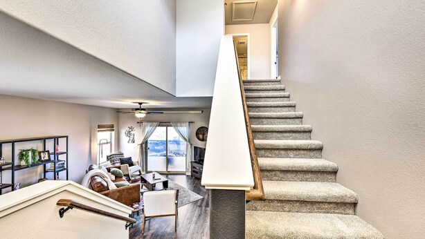A staircase with a handrail leading to a landing, a dining area with a table and chairs, and a view of the outdoors through a large window. - Modern Poncha Springs Townhome w/ Mtn Views! (Salida)