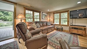 A spacious living room with a brown leather sectional sofa, a wooden coffee table, and a large flat-screen TV mounted on the wall. - Settlers Mountain Retreat: On-site Hikes & Views! (Bryson City)