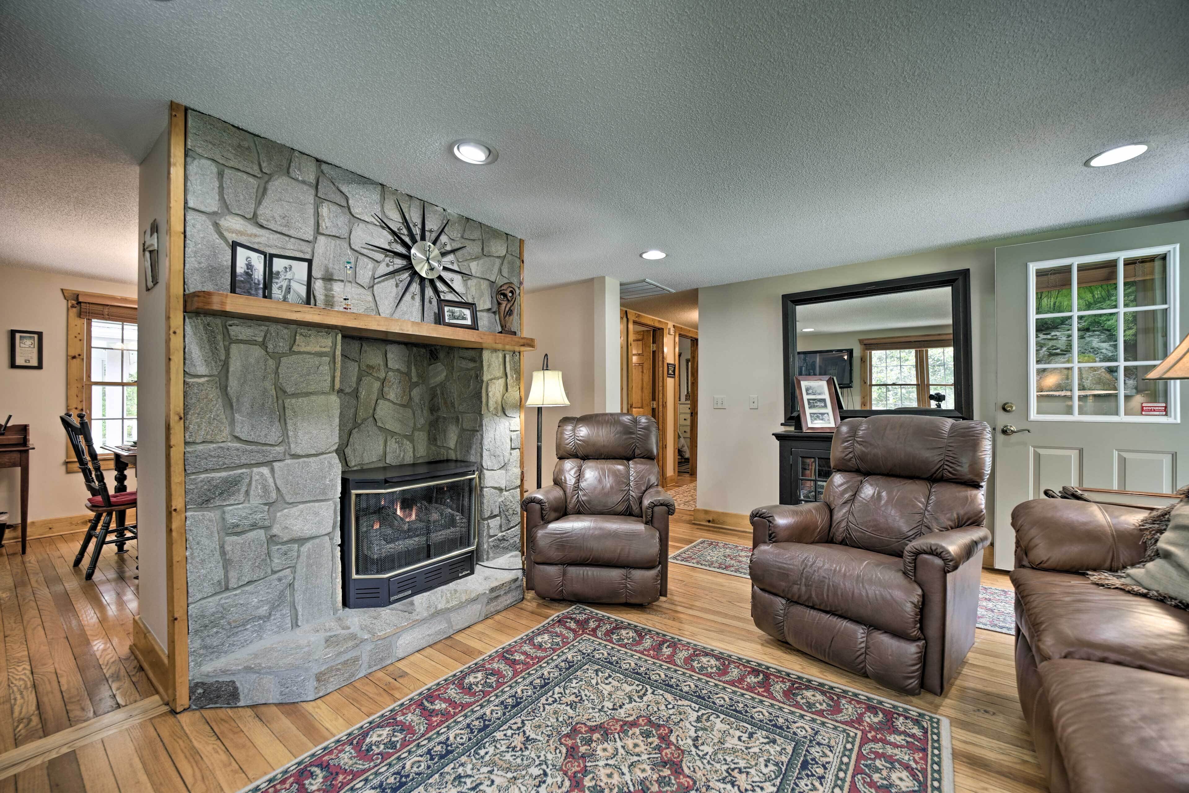 A cozy living room with a stone fireplace, leather recliners, and a large rug.