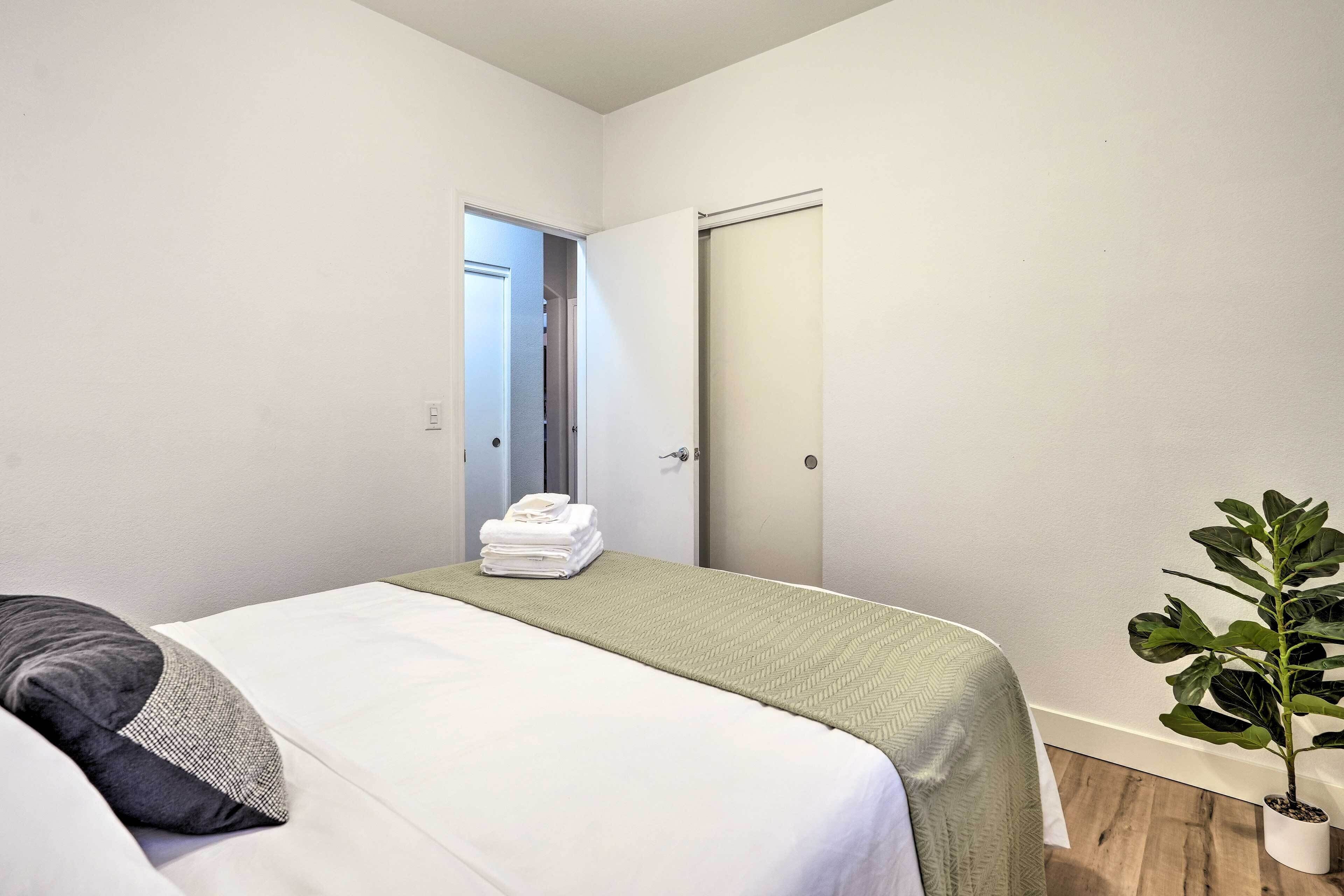 A hotel room with a bed, a green bedspread, a plant, and a door leading to a bathroom.