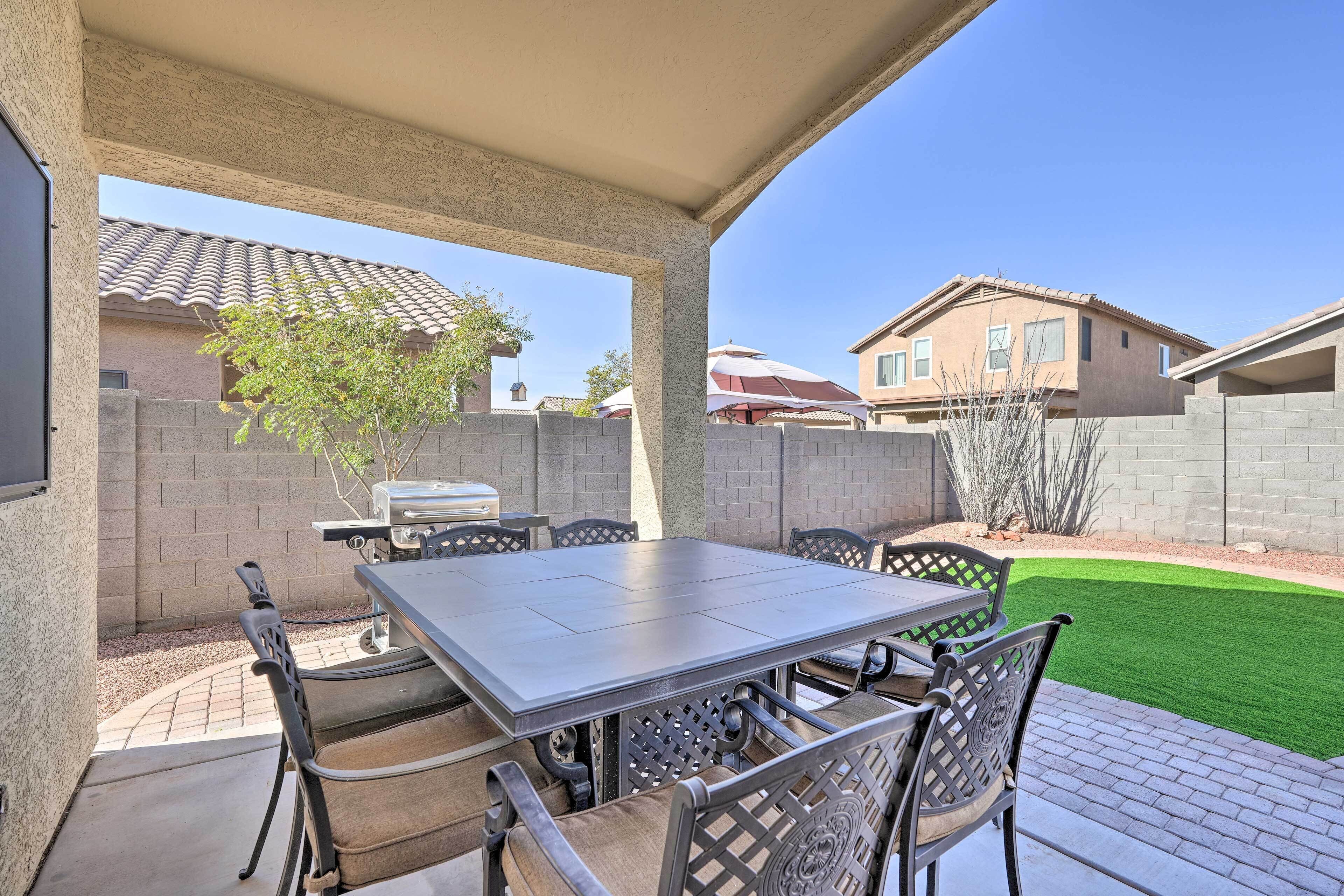 An outdoor patio with a table and chairs, a grill, and a well-maintained lawn.
