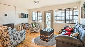 A living room with a fireplace, a sofa, a patterned armchair, a leather couch, and a vintage trunk. - Renovated Cabin w/ Decks, Views, & Fire Pit! (Pikeville)