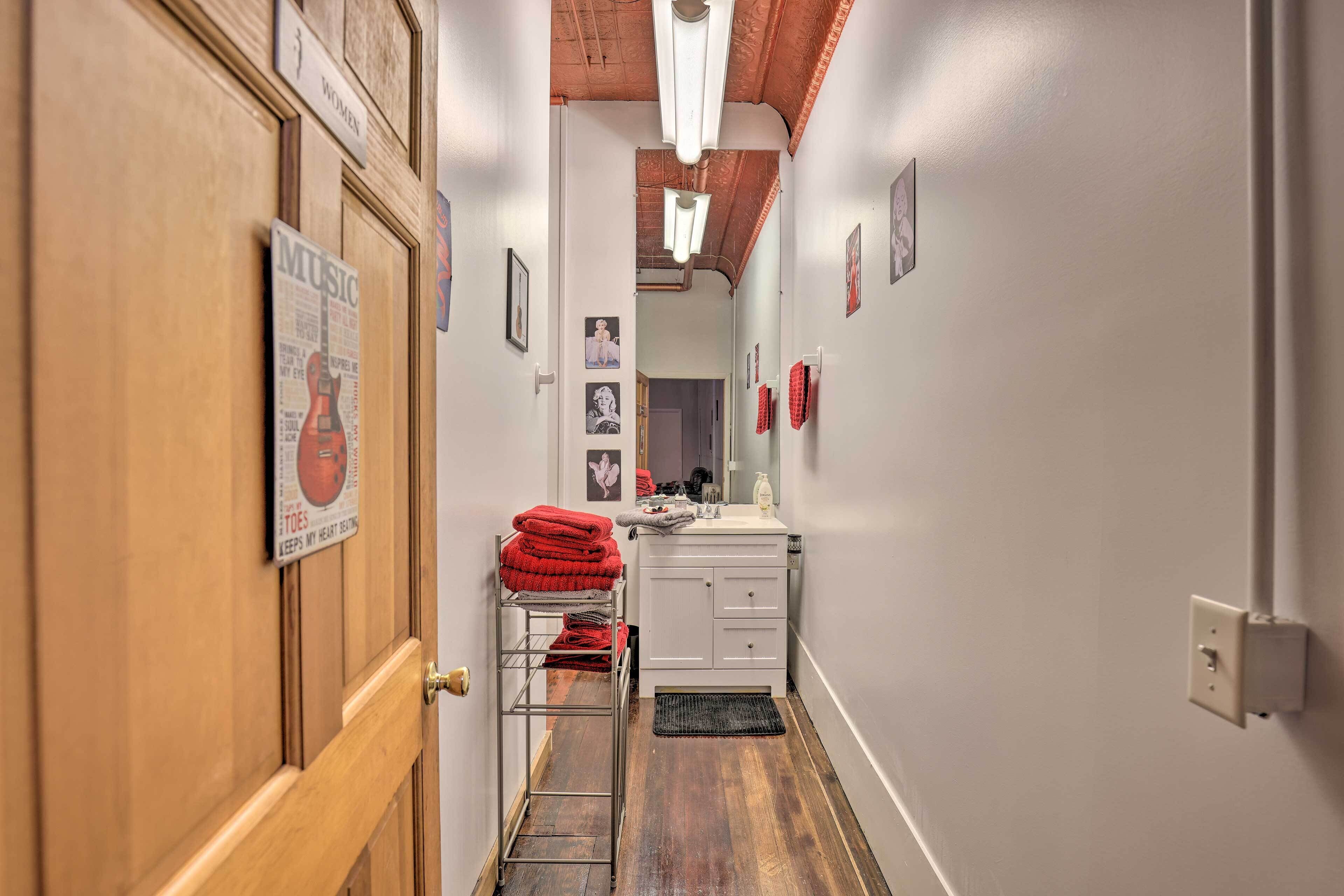 A narrow hallway with a wooden door, a metal rack with red towels, a white sink, and a mirror.