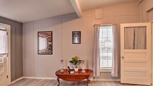 A hallway with a wooden floor, a white door, a window with curtains, and two framed pictures on the wall. - Upstate New York Studio Rental - Pet Friendly (Stanley)