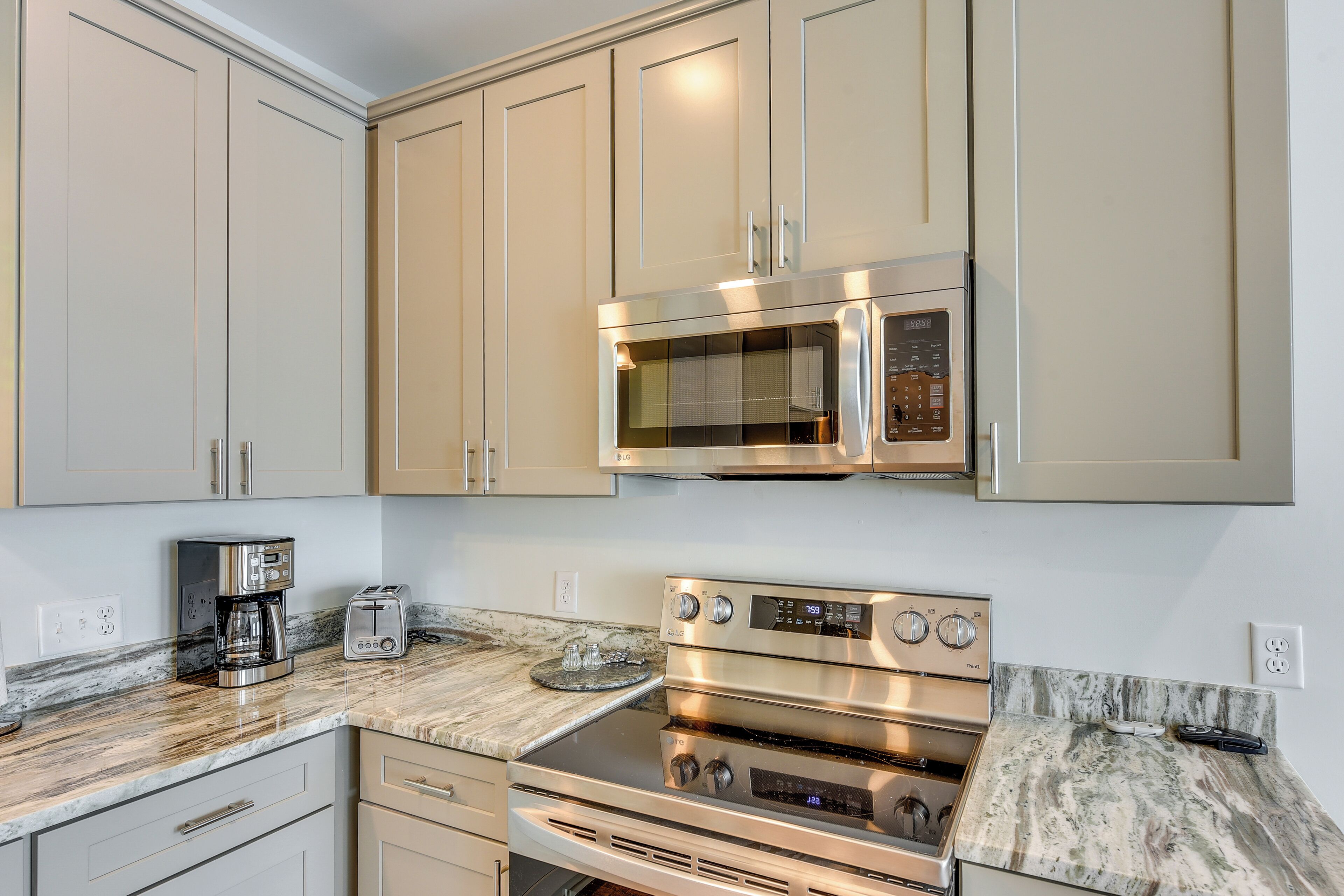 A kitchen with beige cabinets, a stainless steel microwave, a double oven, a coffee maker, and a toaster.