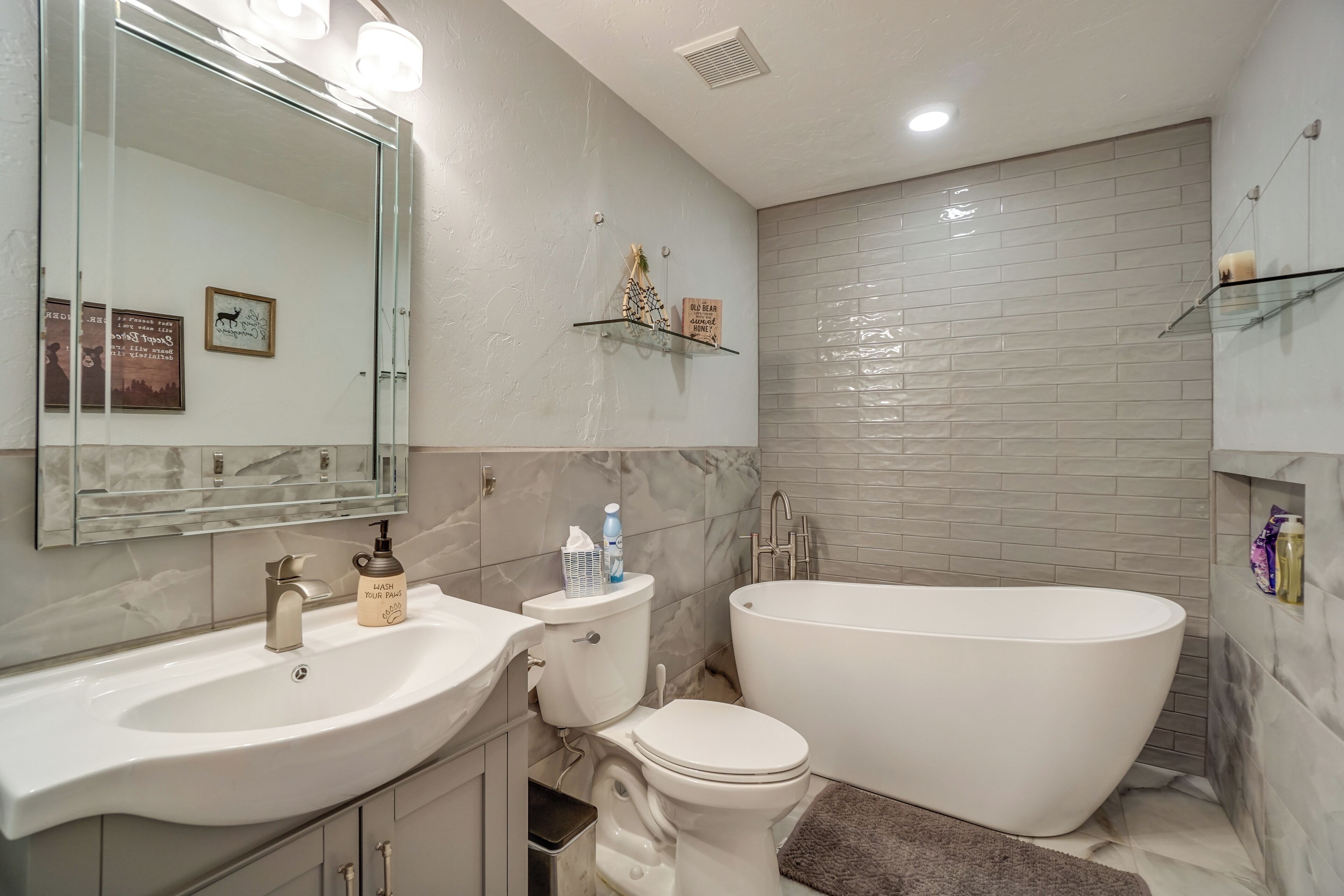 A modern bathroom with a large white bathtub, a sink with a mirror, and a toilet.
