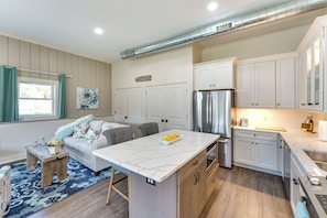 A modern kitchen with white cabinets, a marble island, stainless steel appliances, and a blue patterned rug.