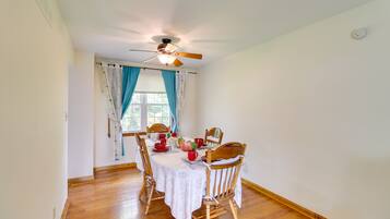 A dining area with a round table, wooden chairs, a ceiling fan, and a window with curtains.