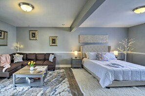 A modern bedroom with a brown sofa, a white bed, and a coffee table with a vase of yellow flowers. - Cozy Port Orchard Home w/ Grill & Fire Pit! (Port Orchard)