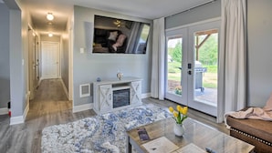 Una sala de estar moderna con chimenea, un televisor de pantalla plana, una mesa de centro con un jarrón de flores y un ventanal corredizo que da a un patio.