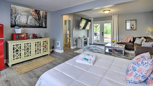 Habitación de hotel moderna con una cama grande, televisor, zona de comedor y vistas al exterior.
