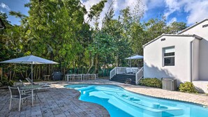A swimming pool with a curved design, surrounded by a patio area with chairs and umbrellas. - Modern Miami Villa w/ Pool Oasis ~ 5 Mi to Beach! (North Miami)