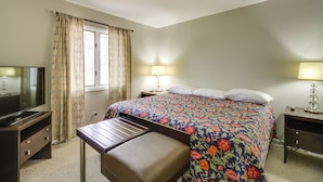 Une chambre d’hôtel comprenant un lit, deux tables de chevet, un téléviseur et un bureau avec une chaise.
