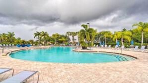 A large, curved swimming pool with lounge chairs and umbrellas around it, surrounded by palm trees and a cloudy sky. - Screened Patio & Resort Perks: Bradenton Condo! (Bradenton)
