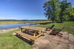 En plats för picknick med ett träbord och stolar, en grill och utsikt över en sjö.