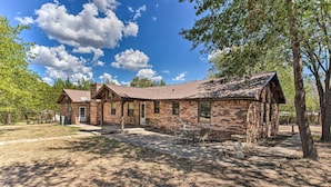 A rustic brick building with a metal roof, a patio with a table and chairs, and a stone birdbath. - Lovely 'anna Fink House' w/ Patio & Fire Pit (Atoka)