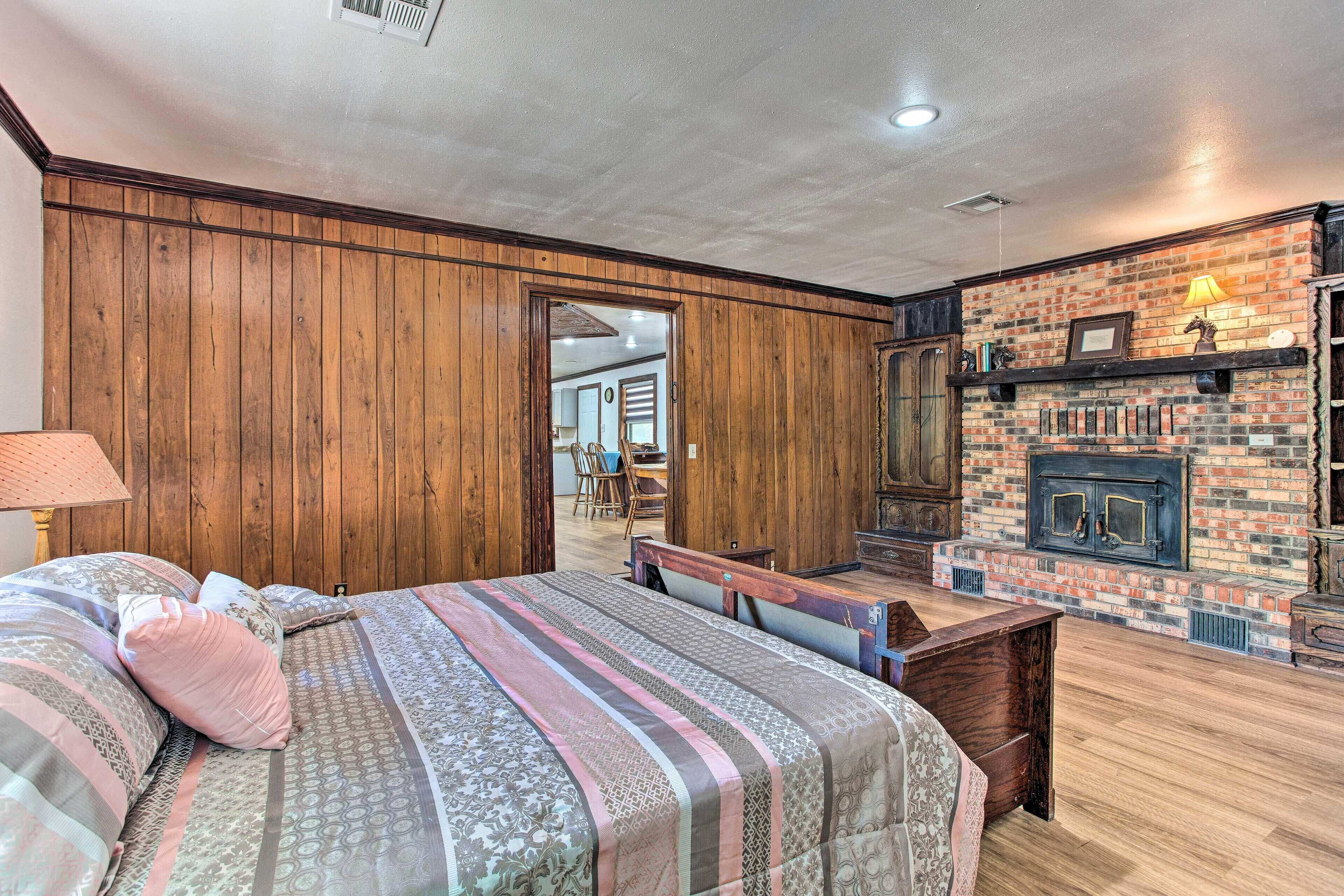 Un dormitorio con pared de paneles de madera, chimenea de ladrillo, cama con ropa de cama estampada y un banco.