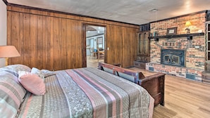 A bedroom with a wooden paneled wall, a brick fireplace, a bed with patterned bedding, and a bench. - Lovely 'anna Fink House' w/ Patio & Fire Pit (Atoka)