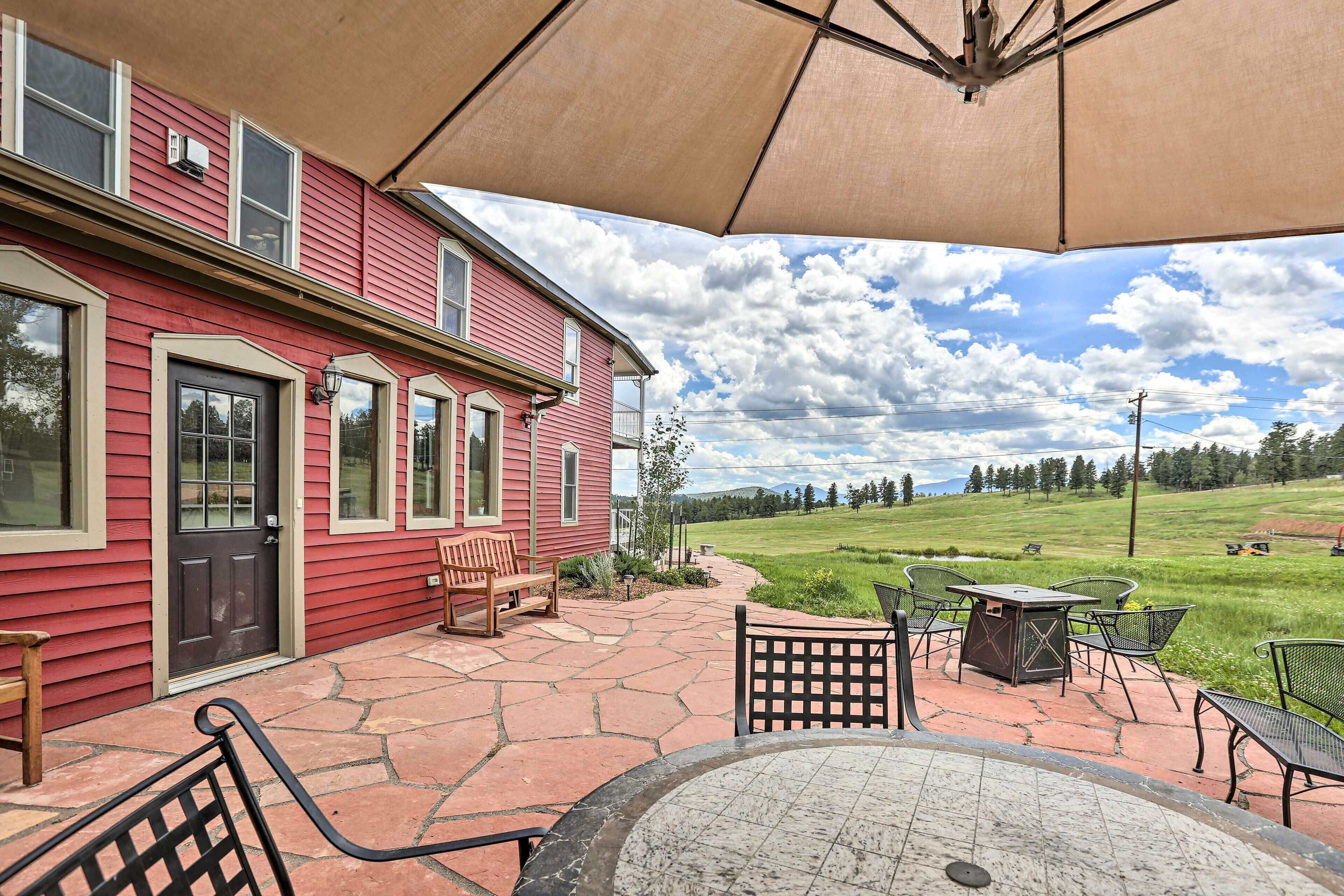 Ein rotes Haus mit Terrasse, Sitzgelegenheiten im Freien und Blick auf ein grünes Feld.