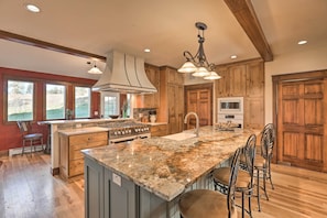 A kitchen with wooden cabinets, a granite island, and a large window. - Mtn View + Group Ready: Conifer Home on 100 Acres! (Conifer)