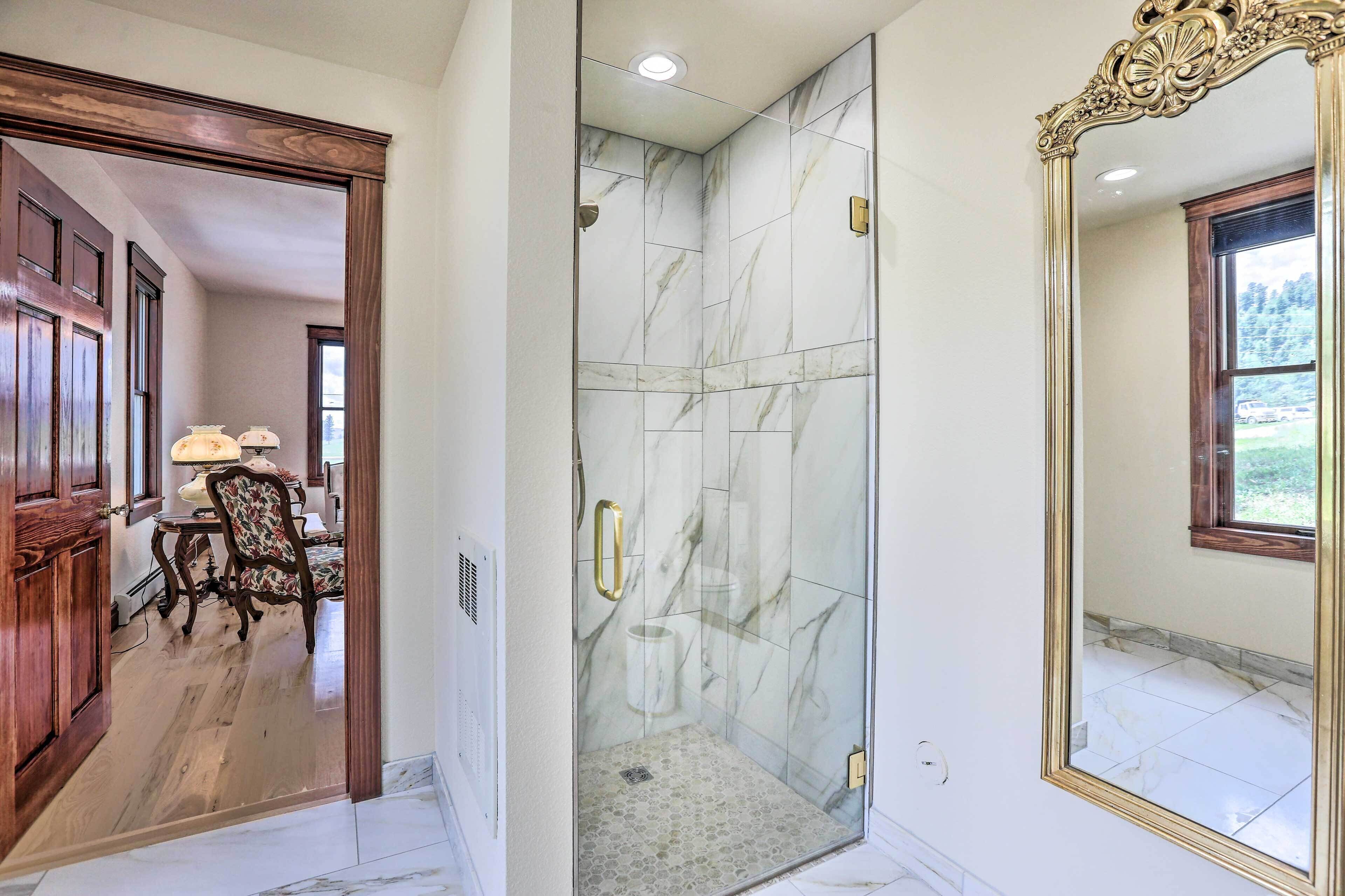 A bathroom with a glass-enclosed shower, marble walls, and a large mirror.