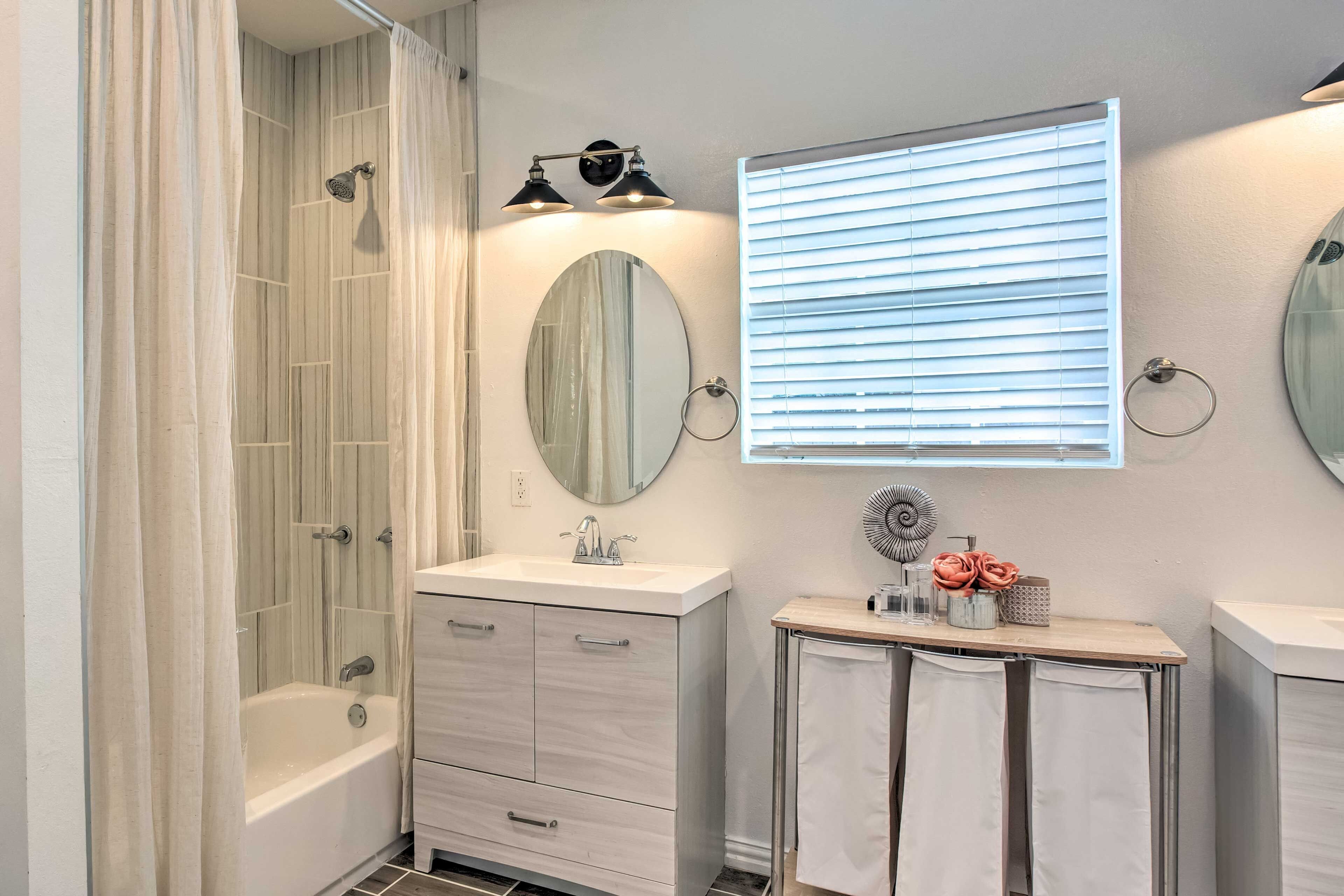 Un baño moderno con bañera, tocador con espejo y ventana con persianas.