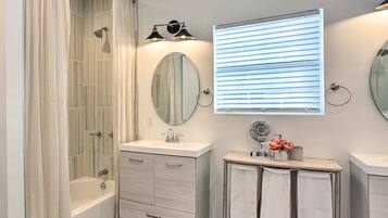Un baño moderno con bañera, tocador con espejo y ventana con persianas.