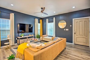 A modern living room with a sofa, TV, ceiling fan, and large windows with curtains. - 4 Mi to Dtwn Dallas: Home w/ Fire Pit + Gazebo (Dallas)