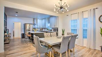 A modern kitchen with white cabinets, a central island, and a dining area with a light-colored table and grey chairs.