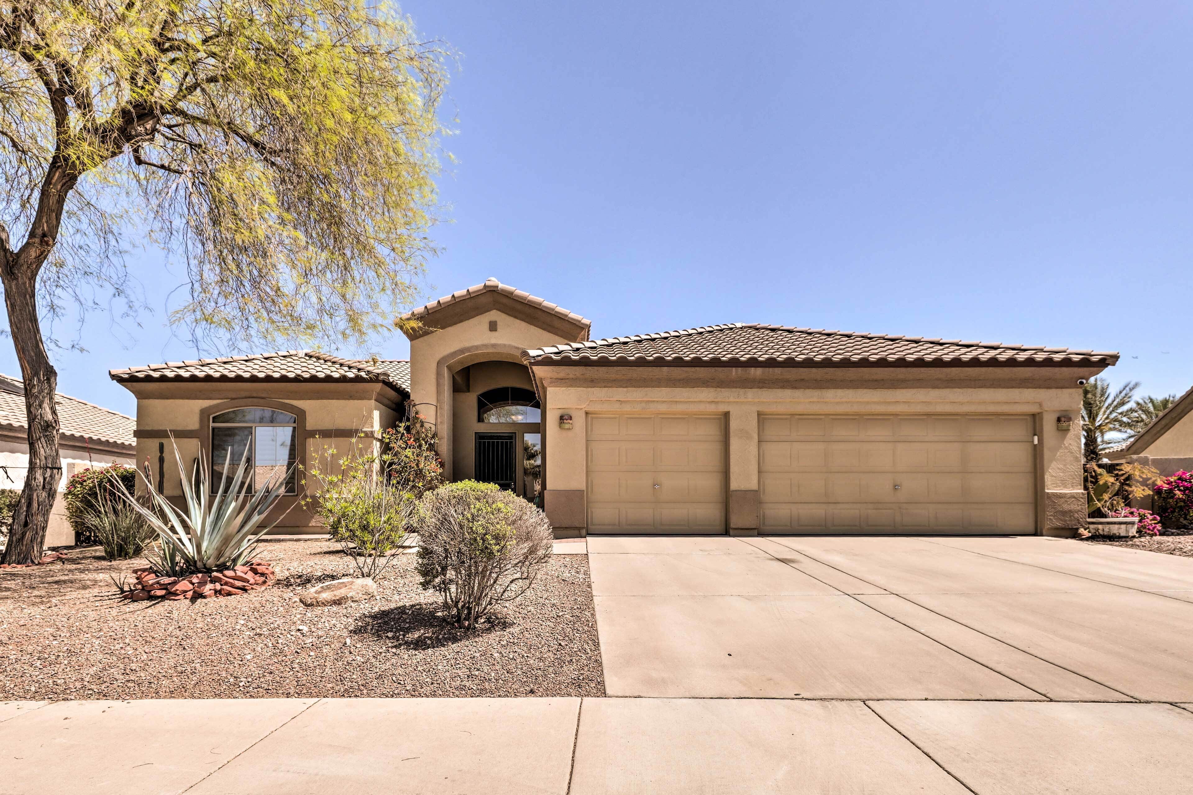 A residential house with a garage, a driveway, and landscaping including a tree and a small bush.
