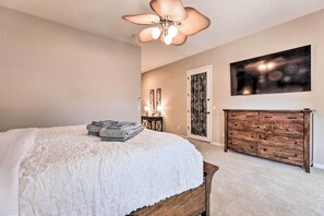 A bedroom with a bed, a wooden dresser, a ceiling fan, and a wall-mounted TV.
