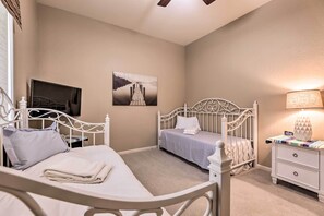A bedroom with two beds, a TV, a painting, and a bedside lamp. - Sun-drenched Home w/ Private Pool in Goodyear (Goodyear)