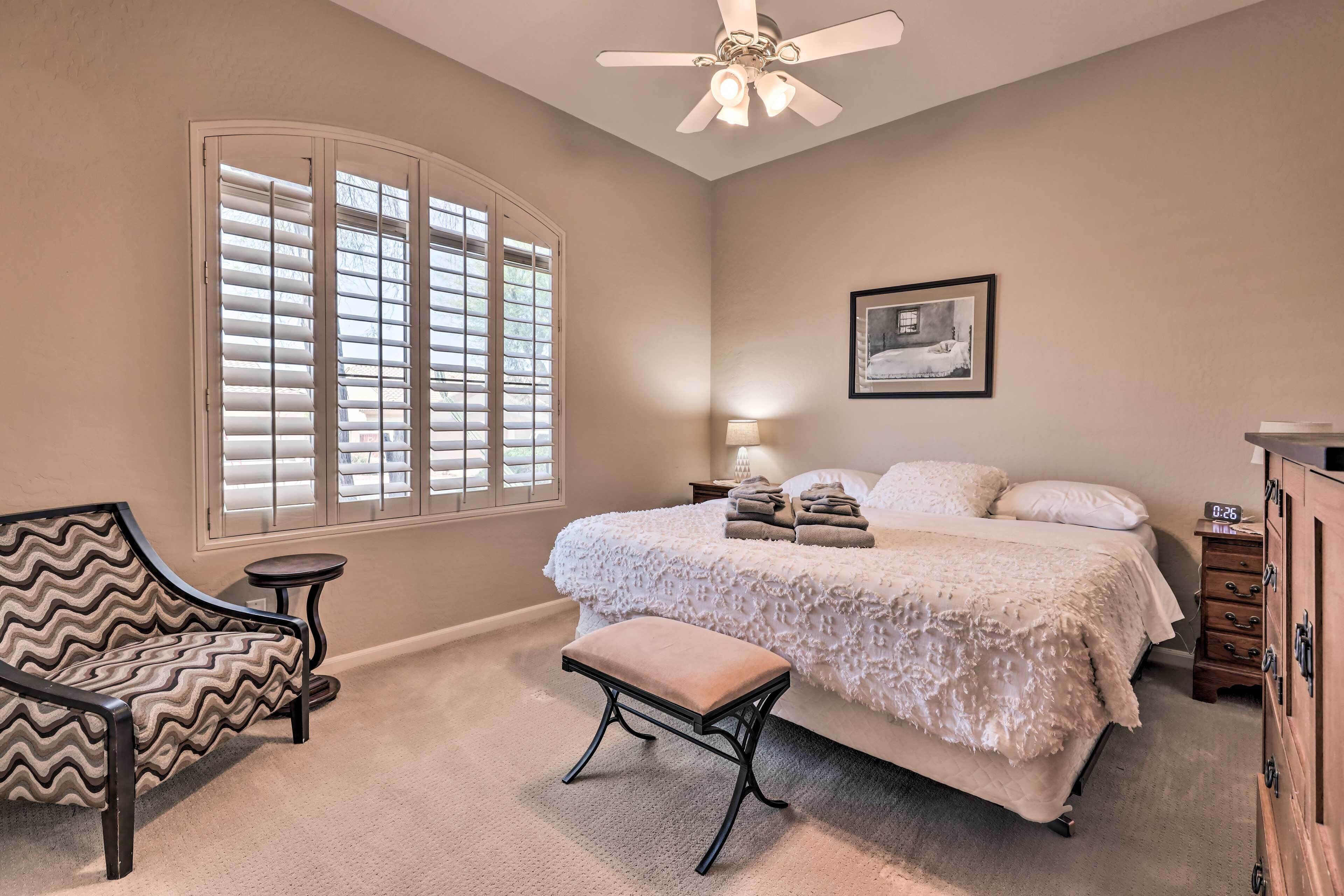 A bedroom with a bed, a chair, an ottoman, a nightstand, and a dresser.