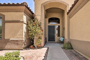A building with a covered patio, a door with a metal gate, and a small seating area with a chair and a handbag. - Sun-drenched Home w/ Private Pool in Goodyear (Goodyear)