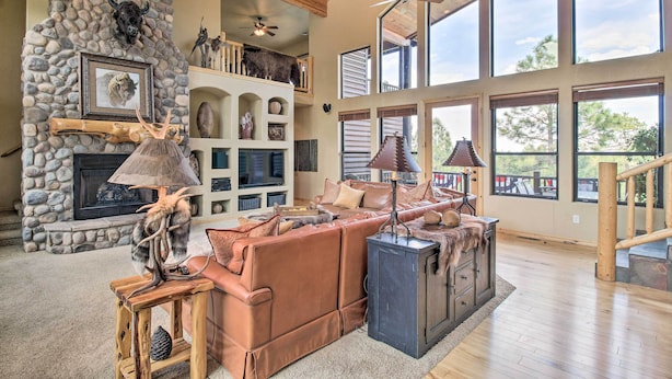 A spacious living room with a stone fireplace, leather sofa, and a large window overlooking a deck.