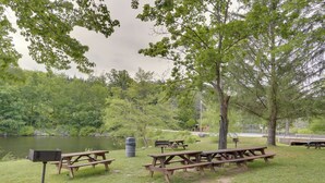 A picnic area with several wooden picnic tables and benches, surrounded by trees and a lake. - Poconos Retreat w/ Pool and Lake Access (Lake Ariel)