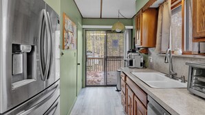 A kitchen with a stainless steel refrigerator, wooden cabinets, a sink, and a window overlooking a deck. - Poconos Retreat w/ Pool and Lake Access (Lake Ariel)