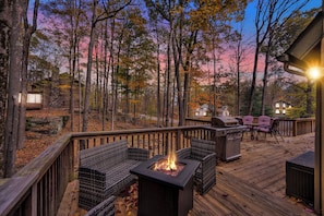 A deck with outdoor furniture, a fire pit, and a grill, surrounded by trees and a wooden deck. - Poconos Retreat w/ Pool and Lake Access (Lake Ariel)