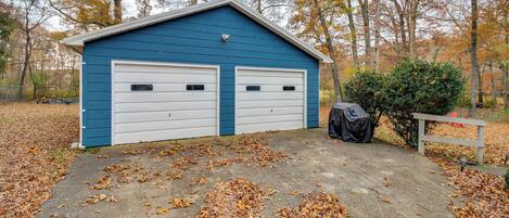 A blue garage with two white doors, surrounded by fallen leaves and trees.