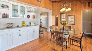 A wooden-paneled dining area with a glass table and chairs, white cabinetry, and framed artwork on the walls.