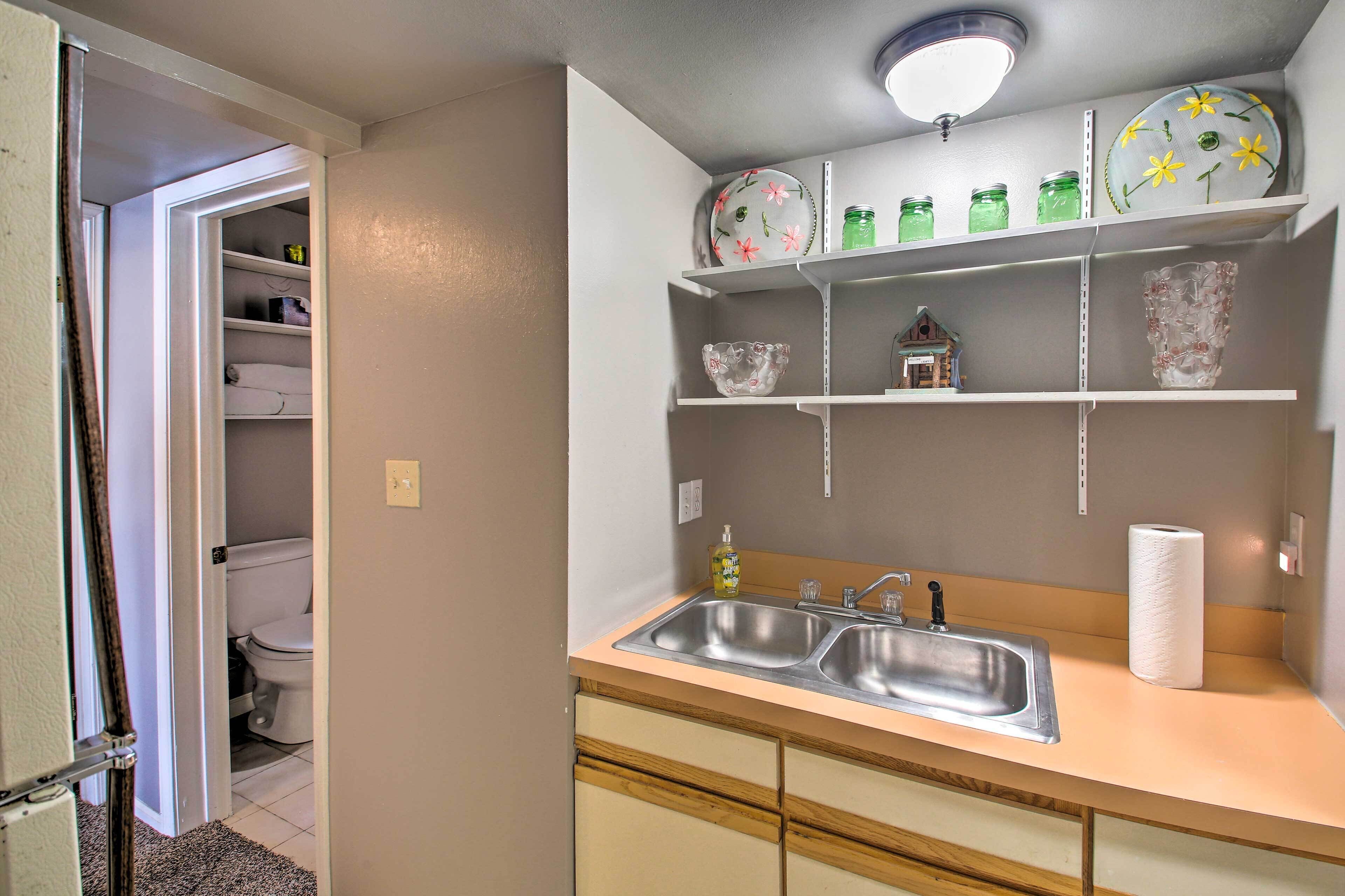 Une cuisine équipée d’un évier, d’étagères ornées d’objets décoratifs et de toilettes visibles dans la pièce adjacente.
