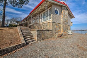 A stone building with a red roof, a set of stairs leading to a porch, and a view of a body of water in the background.
