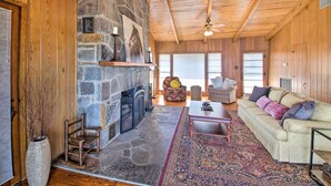 A spacious living room with a stone fireplace, wooden ceiling, and a large window.