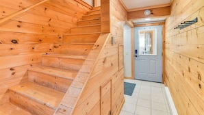 Un escalier en bois mène à une porte dotée d’une petite fenêtre, un luminaire est fixé au plafond et un étagère en métal est accrochée au mur.